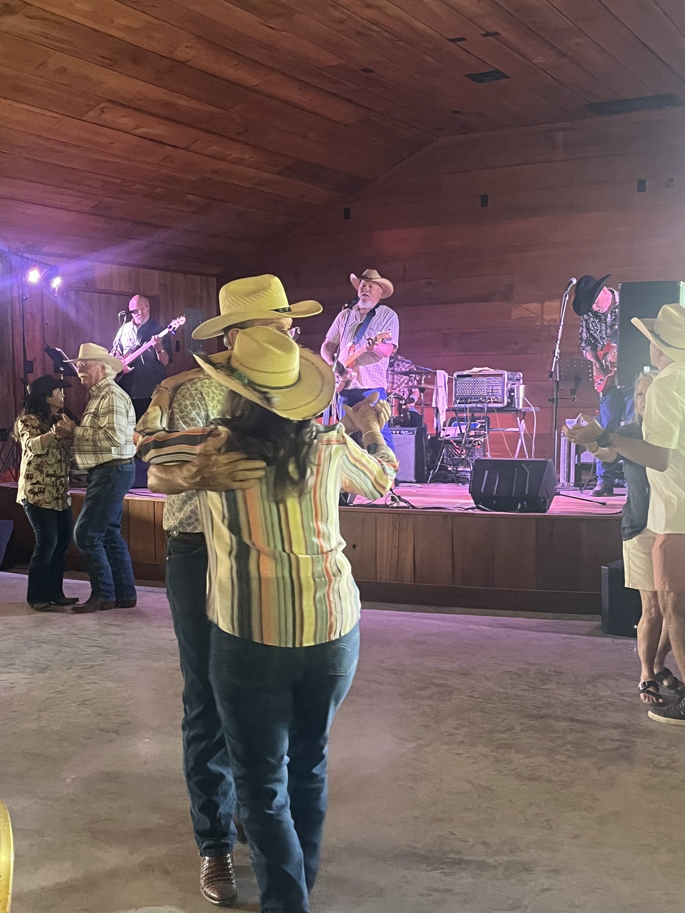 Couples in cowboy hats two-stepping on the dance floor at The Longhorn while a band plays on stage.