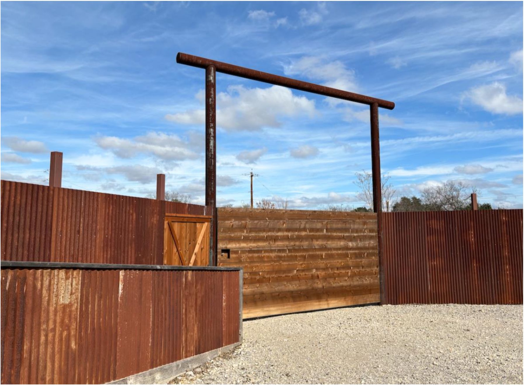 The corten steel entrance gate framed against a blue Texas sky.